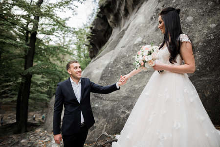 Beautiful gorgeous bride posing to groom and having fun near at mountains with amazing view, space for text, wedding coupleの写真素材