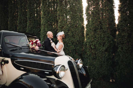 Happy newlywed couple, man and wife kissing near stylish retro carの写真素材