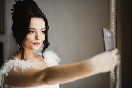 A sweet smiling bride in a light interior makes selfie on the phoneの写真素材