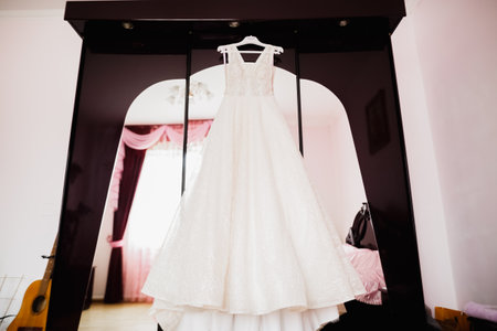 The perfect wedding dress with a full skirt on a hanger in the room of the brideの写真素材