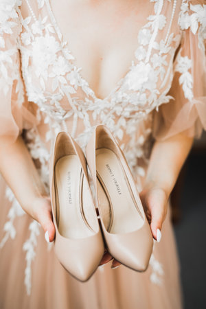 Beautiful luxury bride in elegant white dress holds wedding shoes in the handsの写真素材
