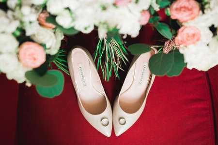 Pair of elegant and stylish bridal shoes with wedding rings and a bouquet of roses and other flowersの写真素材