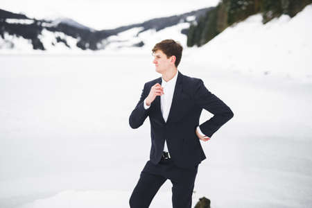 Young man looking away, back view, lake and winter mountains on backgroundの写真素材