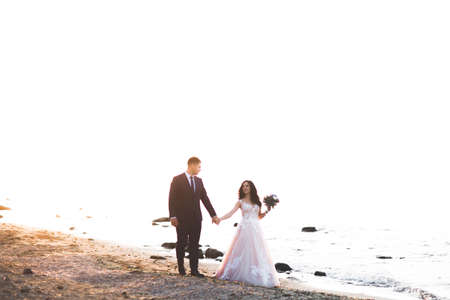 Wedding couple, groom, bride with bouquet posing near sea and blue skyの写真素材