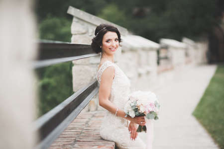 Beautiful brunette bride in elegant white dress holding bouquet posing neat treesの写真素材
