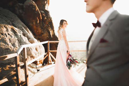 Young newly wed couple, bride and groom kissing, hugging on perfect view of mountains, blue skyの写真素材