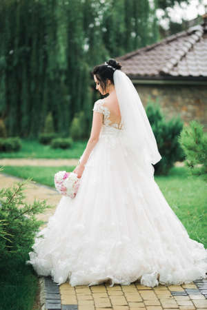 Beautiful bride in elegant white dress holding bouquet posing in parkの写真素材