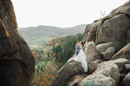 Beautiful gorgeous bride posing to groom and having fun near at mountains with amazing view, space for text, wedding coupleの写真素材