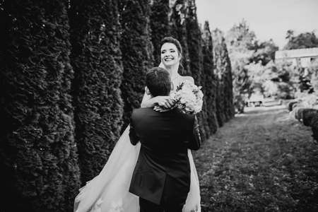 Stylish couple of happy newlyweds walking in the park on their wedding day with bouquetの写真素材