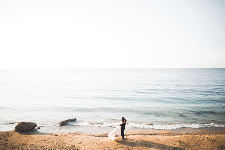 Wedding couple, groom, bride with bouquet posing near sea and blue skyの写真素材