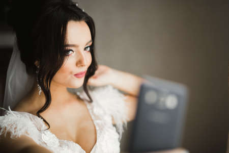 A sweet smiling bride in a light interior makes selfie on the phoneの写真素材