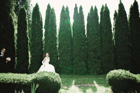 Stylish couple of happy newlyweds.Bride running from groom in the park on their wedding day with bouquetの写真素材