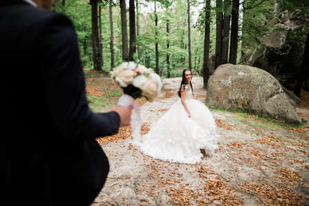 Stylish couple of happy newlyweds. Bride running from groom in the park on their wedding day with bouquetの写真素材