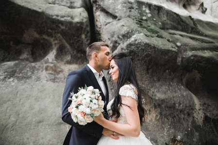 Beautiful young wedding couple posing with bouquet of flowers in handsの写真素材
