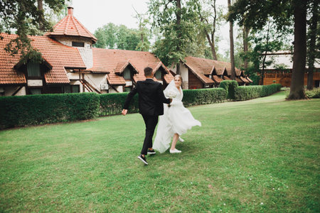 Stylish couple of happy newlyweds. Bride running from groom in the park on their wedding day with bouquetの写真素材