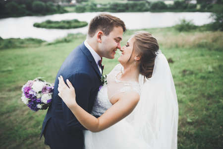 Romantic, fairytale, happy newlywed couple hugging and kissing in a park, trees in backgroundの写真素材