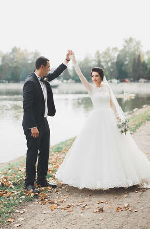 Stylish couple of happy newlyweds walking in the park on their wedding day with bouquetの写真素材