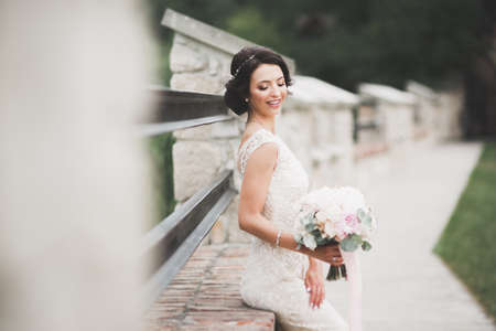 Beautiful brunette bride in elegant white dress holding bouquet posing neat treesの写真素材