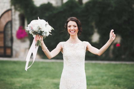 Beautiful brunette bride in elegant white dress holding bouquet posing neat treesの写真素材