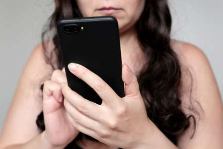 Sexy woman with long curly hair using smartphone. Concept of online communication, sms, social mediaの写真素材