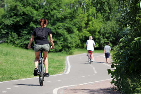 Woman in shorts riding on a bicycle on a path in a green park, selective focus. Girl cyclist, summer...