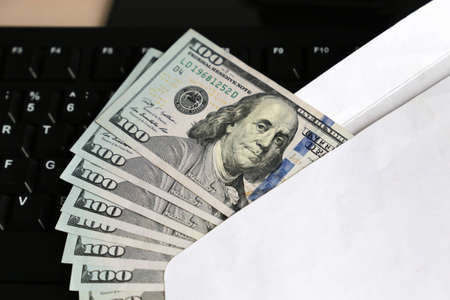 US dollars in white envelope on PC keyboard background. Income, wages or bribe concept