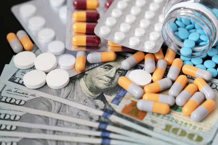 Pills and capsules on US dollar bills. Concept of health care, pharmaceutical business, drug prices in United States, pharmacy, medicine and economicsの写真素材