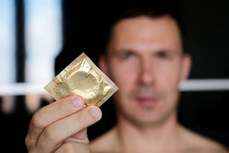 Condom in male hands close up, safe sex. Man giving condom in package, contraception conceptの写真素材
