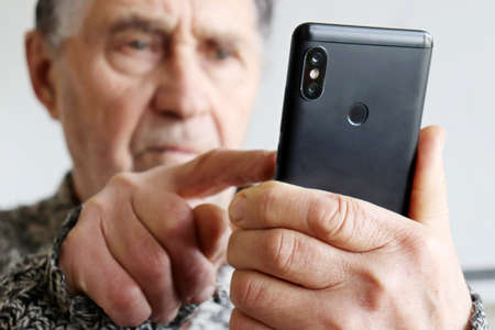 Elderly man using smartphone, mobile phone in male hands close up. Concept of online communication in retirement, sms, social mediaの写真素材