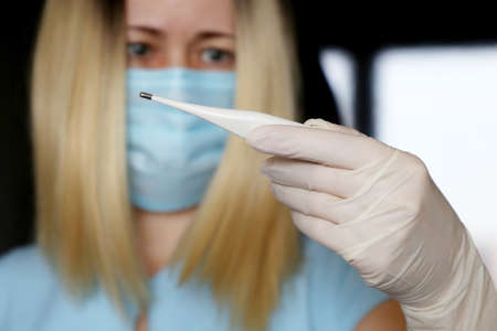 Coronavirus symptoms, woman in medical mask measures body temperature. Doctor with digital...