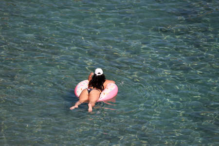 Woman in bikini swimming on inflatable donut ring in a sea. Beach vacation, relax and leisure in...