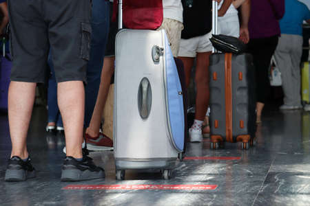 People with luggage standing in a line at airport. Suitcases on wheels and male legs near the...