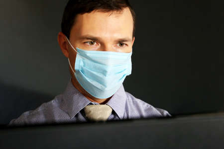 Man in face mask and office clothes sitting at the PC monitor. Safety at work during coronavirus...