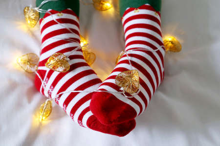 Female legs in Christmas socks with garland and festive lights in heart shape. Concept of romantic...