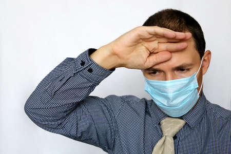 Sick man in face mask and office clothes holding his forehead. Safety at work during coronavirus...