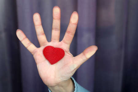 Female hand with red knitted heart on the window glass. Quarantine during the covid-19 coronavirus epidemicの写真素材