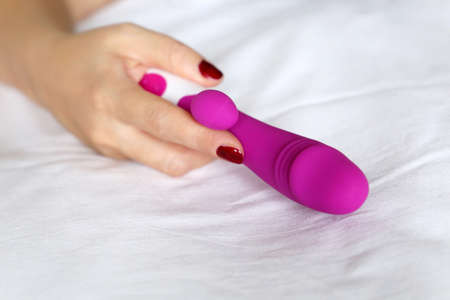 Dildo in female hand close up. Woman on a bed with purple silicone vibrator for sex games