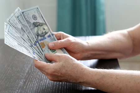Elderly woman with US dollars in wrinkled hands close up. Concept of pension payments, savings at...