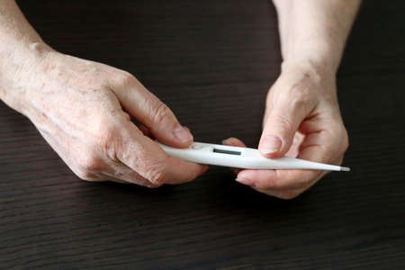 Elderly woman measuring body temperature, concept of fever,  virus symptoms. Digital thermometer in...