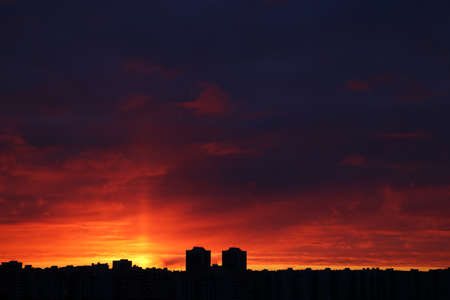 Sunset over city, scenic view. Setting sun and orange sky with dark dramatic clouds above...