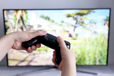 Gamepad in female hands closeup on TV screen background, gaming addiction concept. Girl gamer...