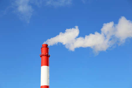 Factory chimney on blue sky background with white smoke. Concept of steam plant, air pollution,...