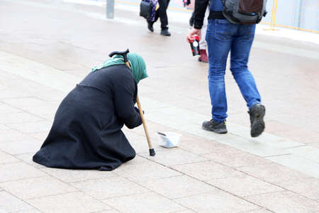Beggar old woman asks for alms sitting on a city street. Poverty, homeless and begging concept