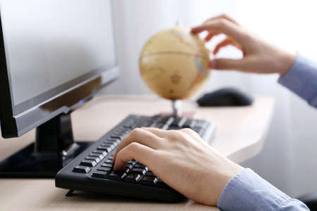 Man with globe sitting at PC keyboard. Concept of choosing travel tourの写真素材