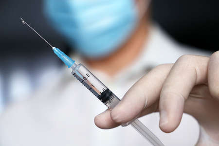 Syringe in doctor hand, man in medical mask and protective gloves preparing to injection. Concept of vaccination during   pandemicの写真素材