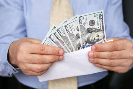 US dollars in male hands close up, man in business clothes with money in white envelope. Concept of cash, income, bribe or salaryの写真素材