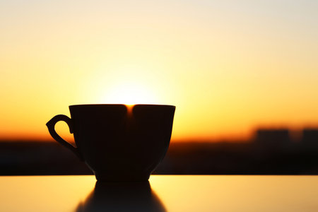 Silhouette of coffee cup on sunrise background, fresh start in the morning. Cozy atmosphere, city view from the windowの写真素材
