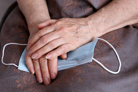 Wrinkled hands of elderly woman with medical face mask. protection for old peopleの写真素材
