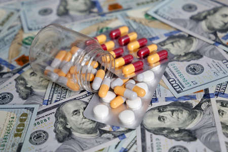 Pills and capsules in a bottle on US dollars bills. Concept of health care in USA, pharmaceutical...