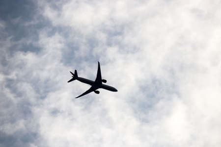 Silhouette of airplane flying in blue sky with white clouds. Passenger plane at flight, travel conceptの写真素材